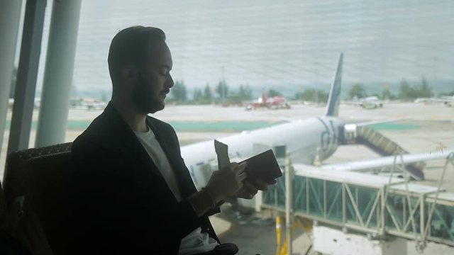At the airport traveler checks tickets and passport at the window. A bearded businessman, while waiting for an air flight, looks at documents to obtain a visa for traveling abroad.