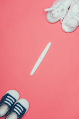 top view of arrangement of  childish shoes and pregnancy test isolated on pink