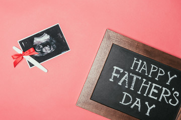 top view of happy fathers day blackboard, ultrasound scan and pregnancy test with ribbon isolated on pink