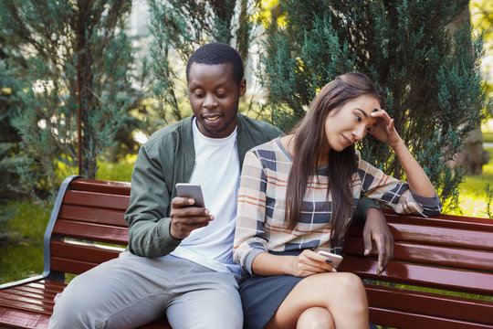 Woman sitting in park with man using smartphone
