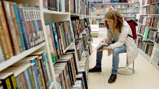 Woman reading a book which she has just removed for a display on a shelf in a bookstore