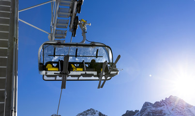 Skiers going up on the chairlift against bright blue sky- ski resort in Italy on sunny winter day