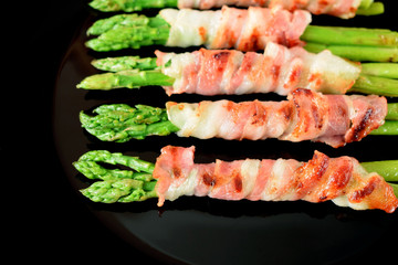 Green asparagus wrapped into smoked bacon on a black plate