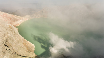 Crater with acidic crater lake Kawah Ijen the famous tourist attraction, where sulfur is mined. Extraction of sulfur in the crater of a volcano. Sulfur gas, smoke.