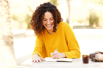young woman sitting at table writing in diary - Powered by Adobe