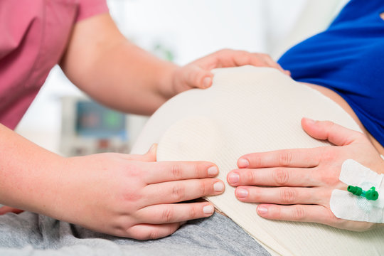 Midwife or nurse in delivery room feeling baby belly of pregnant woman