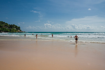 Tourists enjoying the waves and crystal clear water of Kata Beach or Kata Yai in Phuket, Thailand.