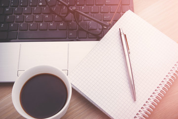 Open laptop, glasses, cup with coffee, notepad and pen on woodden table
