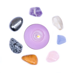 Lavender tea light candle surrounded by set of seven healing chakra stones for crystal healing,...