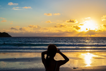 The rear view silhouette of a young woman looking at the horizon during a sunset on the beach. 