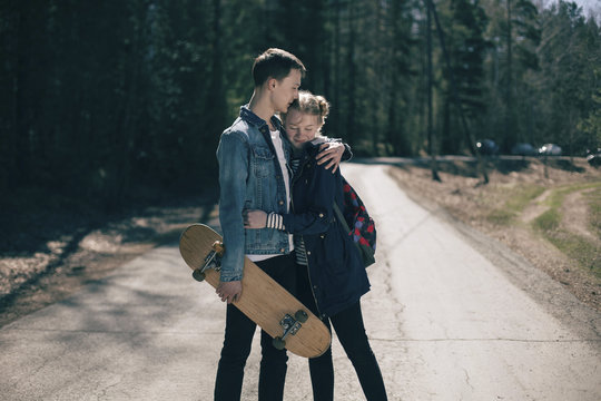 Caucasian couple with skateboard hugging in road