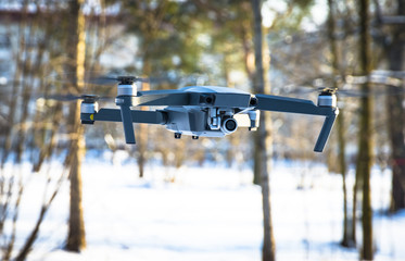 Drone flying in the blue sky, unmanned copter flight over blurred trees forest background