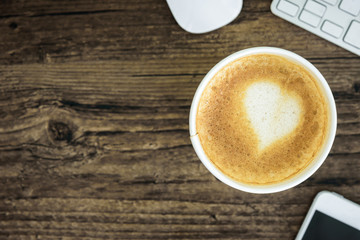 A latte coffee with art heart milk on the brown wood desk table from top view and copy space. Flat lay with desk, business and valentine concept.