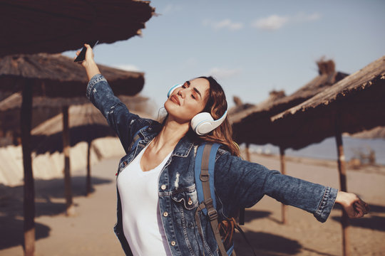 Beautiful young woman listens to music via smartphone and headphones on a sunny day