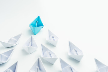 Leadership concept with blue paper ship leading among white on white background.