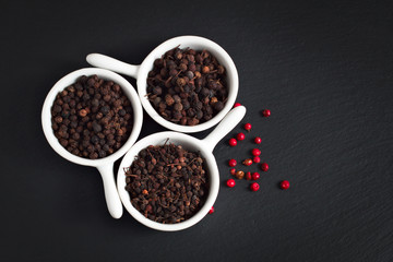 Food Concept 4 kind of dried peppers spices Indian, Madagascar, Indonesian in white ceramic cups and pink peppercorn on black slate stone plate with space for text