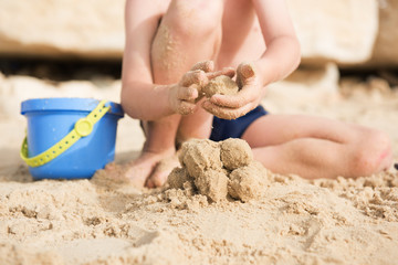 a little boy sits on the beach in the sand and sculpts sand lumps