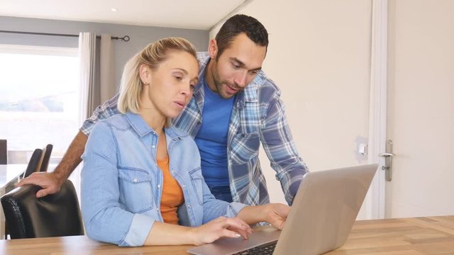cheerful young couple at home shopping and buying online on internet with laptop computer