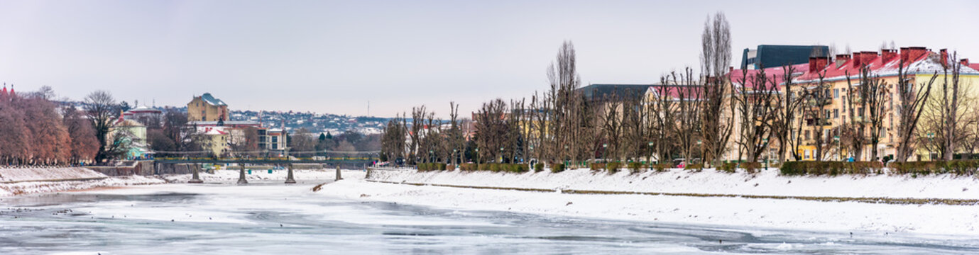 panorama of winter cityscape on the river Uzh. lovely travel background with Kyiv embankment, pedestrian bridge and some architecture of central part of old town Uzhgorod