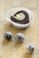 chocolate coconut balls and roulade decorated with shredded coconut on wooden bamboo table