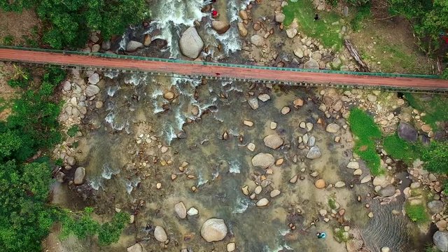Aerial footage of hanging bridge across the river and there are people picnic and camping along the river taken in Kuala Woh Recreational Forest in Tapah Perak, Malaysia.