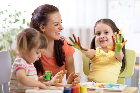 Child girl with painted hands. Kids drawing and coloring with teacher in daycare center.