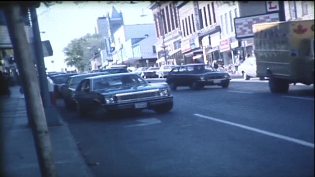 Small city downtown in the 1970's. Shot on film. Cars drive down the street.