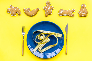 Sport and healthy diet for slimming. Plate, measuring tape and cookies in shape of yoga asans on bright yellow background top view