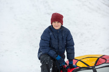 kid sledding from a hill, makes snowballs and snowman on his winter holidays