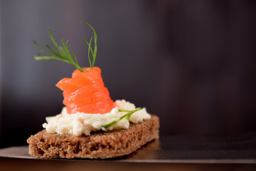 Canape with smoked salmon and cream cheese is lying on a knife on dark wooden background