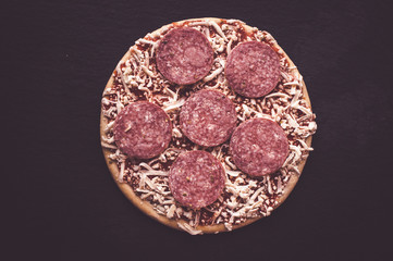 Frozen pepperoni pizza, top view, black background
