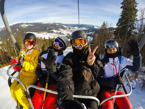 Happy Young Friends Skiers On Ski Lift Ride Up On Ski Slope At Snowy