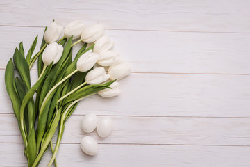 Beautiful white tulips with colorful quail eggs in nest on light gray stone background. Spring and Easter holiday concept with copy space.