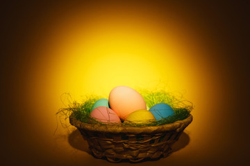 Colorful pastel monophonic traditional painted Easter eggs in basket with green grass on dark yellow background with black shadows, silhouette, light. Copy space for advertisement. With place for text