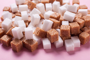 White and brown cane sugar cubes scattered on a pink background. Texture background