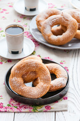 On a wooden table, curd rings on a plate. Background - white, cotton napkins with roses