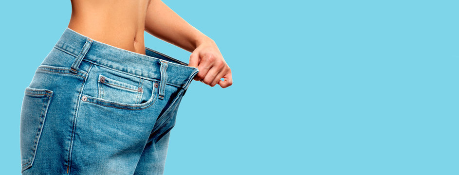 Weight loss. Woman in oversize jeans on blue background
