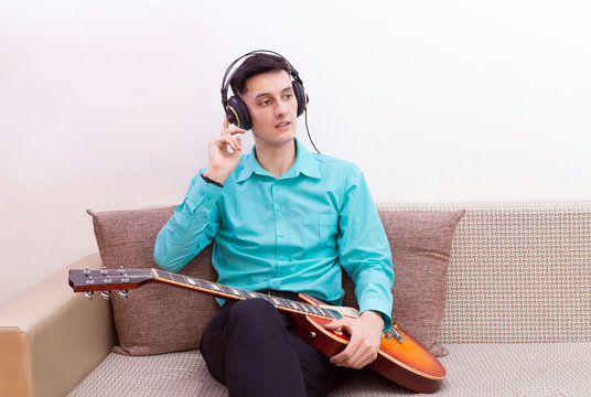 Portrait of a sitting young man in a green shirt holding an electric guitar and listening to music