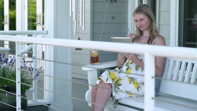 Young woman using digital tablet on porch swing, zoom in