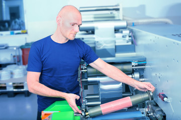 Printer operator next to the printing machine, holding printing cylinder with polymer relief plate...