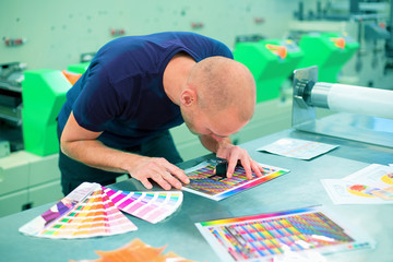 Worker in a printing and press center uses a magnifying glass to check the print quality. Scene...