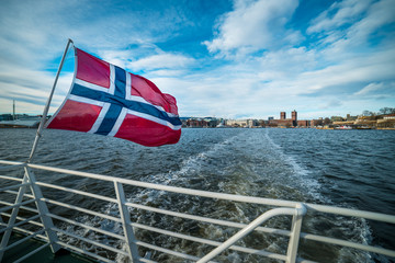 Norwegian flag on ship with Oslo in Norway in the background - obrazy, fototapety, plakaty