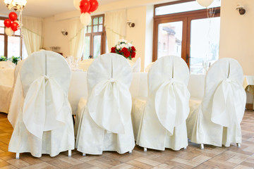 Chairs in white covers with bows. Decoration of chairs for a party.