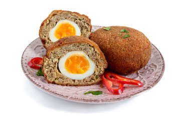 Juicy cutlet from chopped meat stuffed boiled egg on a ceramic plate isolated on a white background.