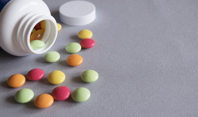 White jar with scattered multicolored of vitamins on a gray fabric