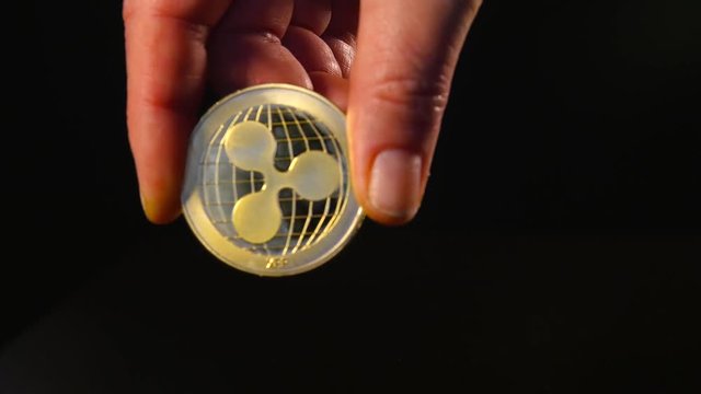 A woman's hand holds a gold coin of ripple. Isolated black background.