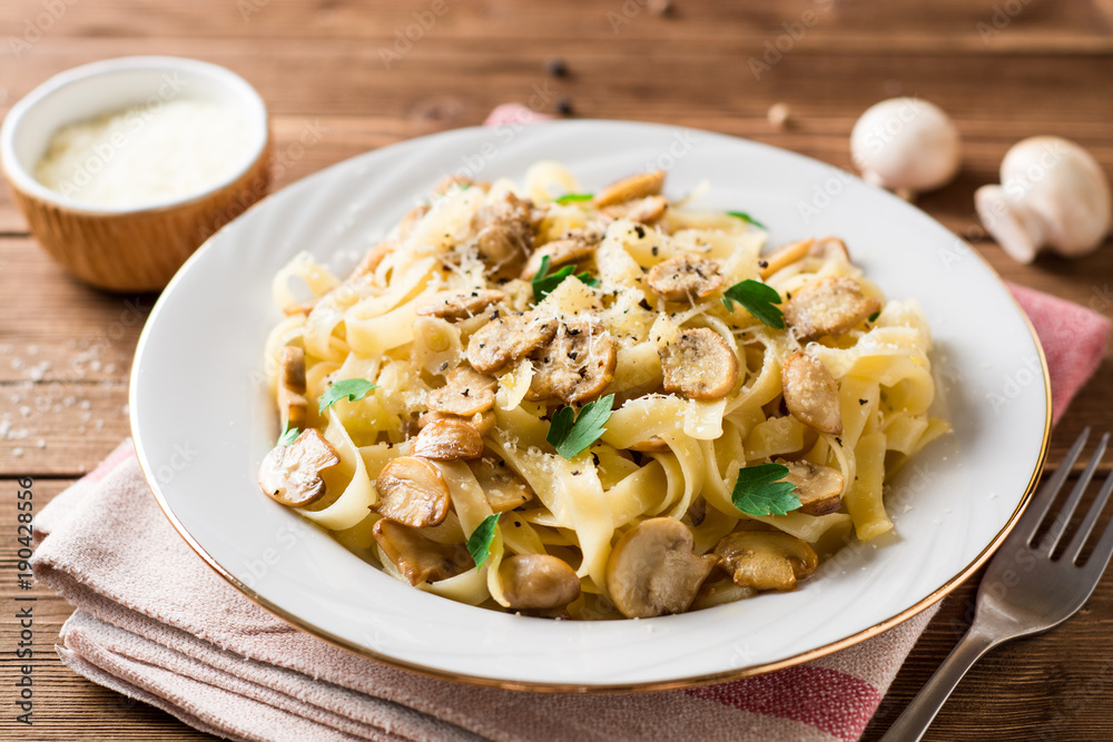 Wall mural Tagliatelle pasta with mushrooms, parsley and Parmesan cheese on wooden table.