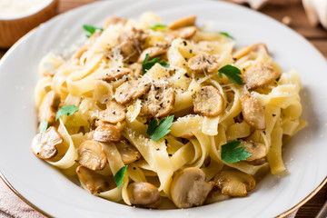 Tagliatelle pasta with mushrooms, parsley and Parmesan cheese on wooden table.
