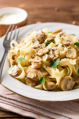 Tagliatelle pasta with mushrooms, parsley and Parmesan cheese on wooden table.