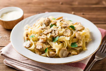 Tagliatelle pasta with mushrooms, parsley and Parmesan cheese on wooden table.